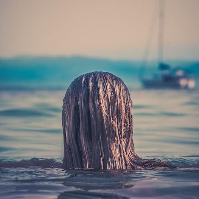 A woman swimming in the sea with boats in the background.